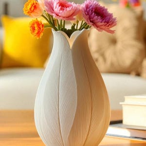 May include: A white ceramic vase with a textured, petal-like design, holding a bouquet of colorful flowers. The flowers include orange, pink, and purple blooms, creating a vibrant contrast against the vase. The vase is on a wooden surface.
