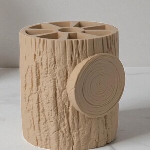 May include: A beige, cylindrical desk organizer designed to resemble a tree stump. The organizer has a textured bark-like exterior and a circular cross-section detail on the side. The top features multiple compartments for pens and pencils.
