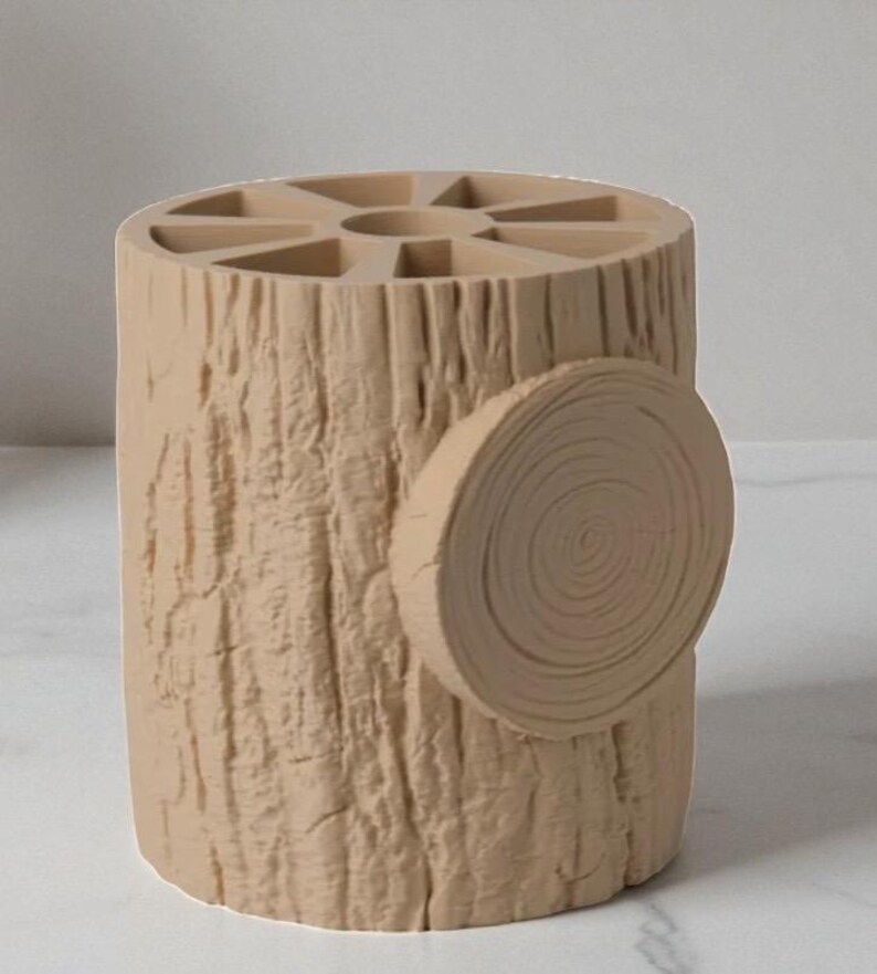 May include: A beige, cylindrical desk organizer designed to resemble a tree stump. The organizer has a textured bark-like exterior and a circular cross-section detail on the side. The top features multiple compartments for pens and pencils.