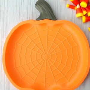 May include: Orange pumpkin-shaped serving dish with a spiderweb design. The dish has a green stem and is filled with candy corn. Perfect for Halloween or fall-themed gatherings.