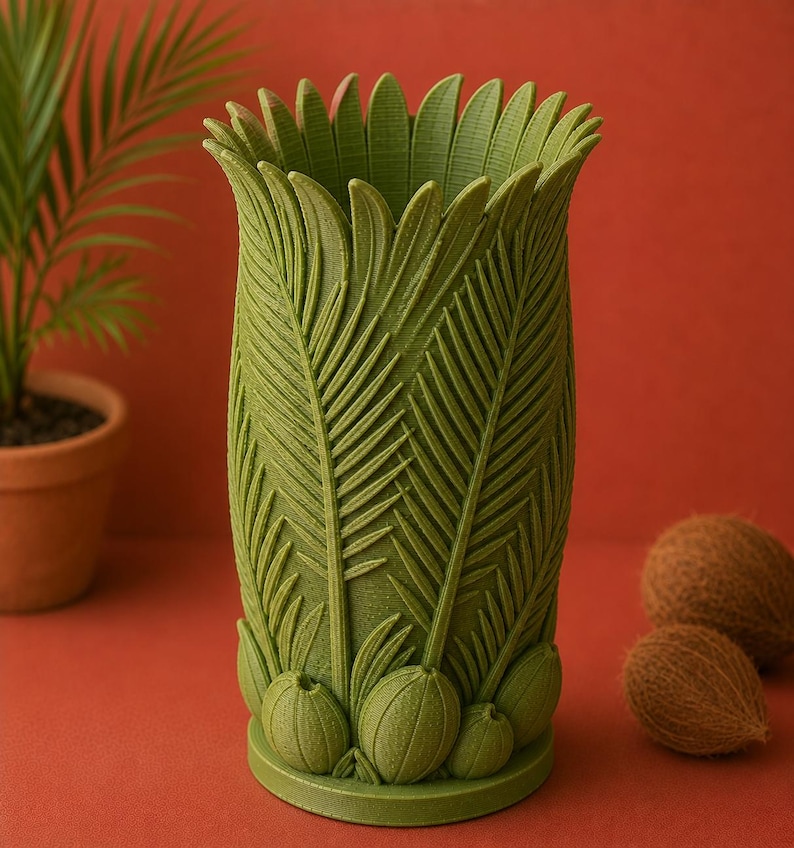 May include: A green decorative vase with a palm leaf design. The vase features detailed leaf and fruit patterns, with a flared top and a round base. The vase is approximately 8 inches tall and is set against a red background.