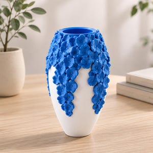 May include: A white ceramic vase with a blue floral design. The vase has a rounded shape with a blue interior and is decorated with cascading blue flowers. The vase is sitting on a wooden table.