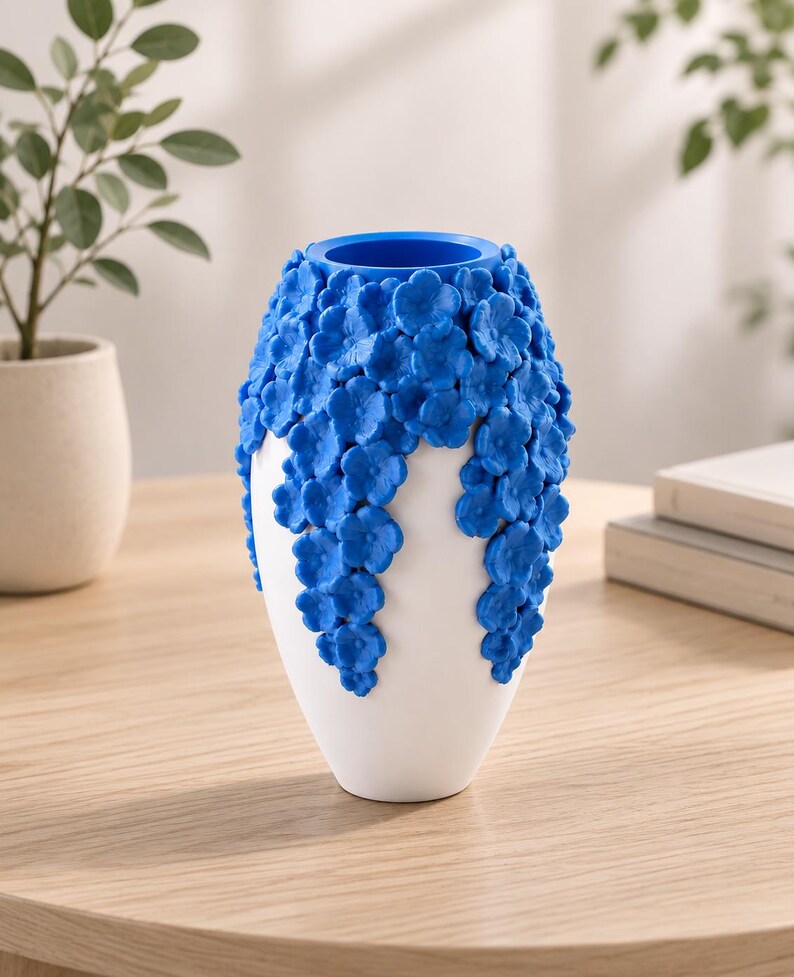 May include: A white ceramic vase with a blue floral design. The vase has a rounded shape with a blue interior and is decorated with cascading blue flowers. The vase is sitting on a wooden table.
