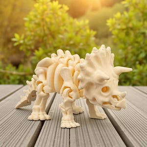 Może przedstawiać: Jasny beżowy model szkieletu dinozaura Triceratops. Model ma trzy rogi, falbanę i szczeg&oacute;łową strukturę szkieletu. Jest ustawiony na szarym drewnianym pokładzie z rozmytym zielonym tłem.