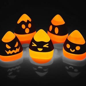 May include: Five orange and black Halloween-themed candy corn shaped light-up decorations. Each candy corn has a different cartoon face.