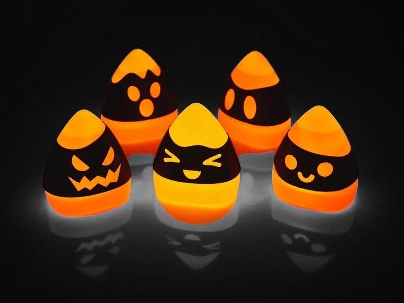 May include: Five orange and black Halloween-themed candy corn shaped light-up decorations. Each candy corn has a different cartoon face.
