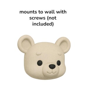 May include: A beige bear-shaped wall mount with black eyes and nose. The text above the bear reads "mounts to wall with screws (not included)". The bear has a textured surface and rounded ears.