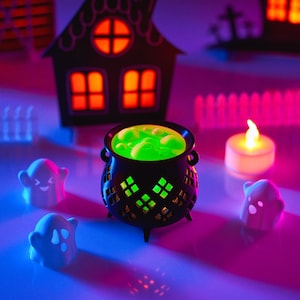 May include: A black cauldron with green liquid inside, surrounded by white ghost figurines and a white candle on a purple and blue surface.