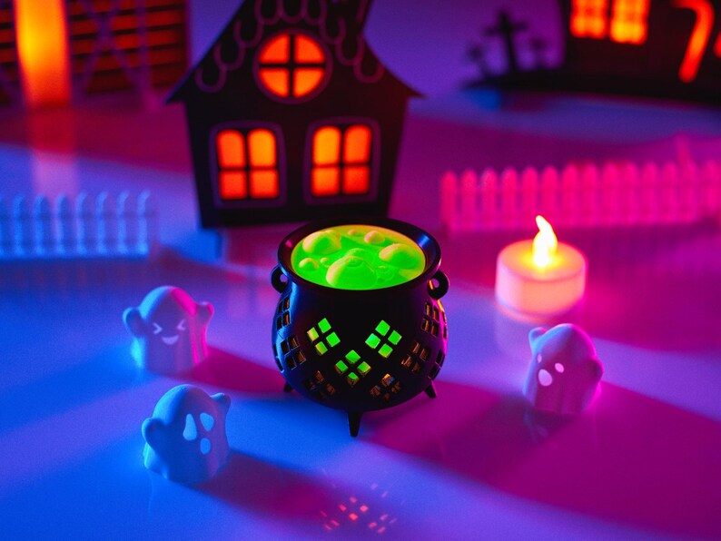 May include: A black cauldron with green liquid inside, surrounded by white ghost figurines and a white candle on a purple and blue surface.