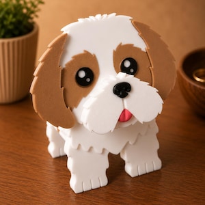 May include: A white and brown dog figurine with large black eyes, a black nose, and a pink tongue. The dog has a layered design and is sitting on a wooden surface. The figurine is a decorative item.