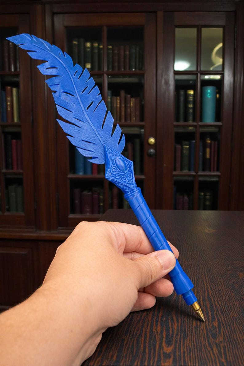 May include: A blue feather pen with a decorative design. The pen has a gold-colored tip and is held in a hand. The background features a wooden bookshelf filled with books.