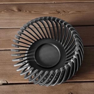 Pu&ograve; includere: Una ciotola decorativa in metallo nero con un design traforato unico. La ciotola presenta una base centrale circolare e supporti verticali curvi che creano un effetto a spirale. La ciotola &egrave; posta su uno sfondo di legno.