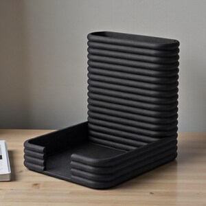 Pu&ograve; includere: Un organizer da scrivania nero con un design a coste unico. Ha una base rettangolare e uno schienale verticale curvo. Il design &egrave; moderno e minimalista, adatto per l'ufficio o la casa.
