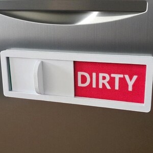May include: A white and red dishwasher magnet with the word "DIRTY" in white block letters. The magnet has a sliding mechanism to indicate the status of the dishes. The background is a stainless steel appliance.