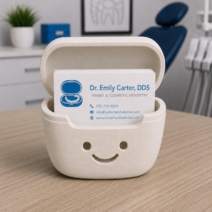 May include: A beige business card holder with a smiling face design, holding business cards for Dr. Emily Carter, DDS, Family & Cosmetic Dentistry. The cards display contact information, including a phone number and website address.