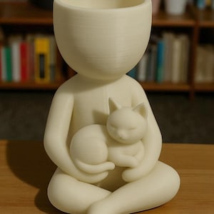 May include: A cream-coloured planter in the form of a person cradling a sleeping cat. The planter has a wide opening for plants. The cat is curled up in the person's lap, creating a charming and comforting design.