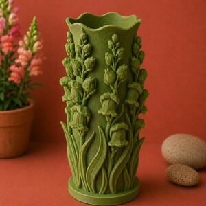 May include: A green vase with a floral design. The vase features detailed relief carvings of flowers and leaves. The vase has a wavy top edge and a cylindrical shape. The background is a solid reddish-orange color.