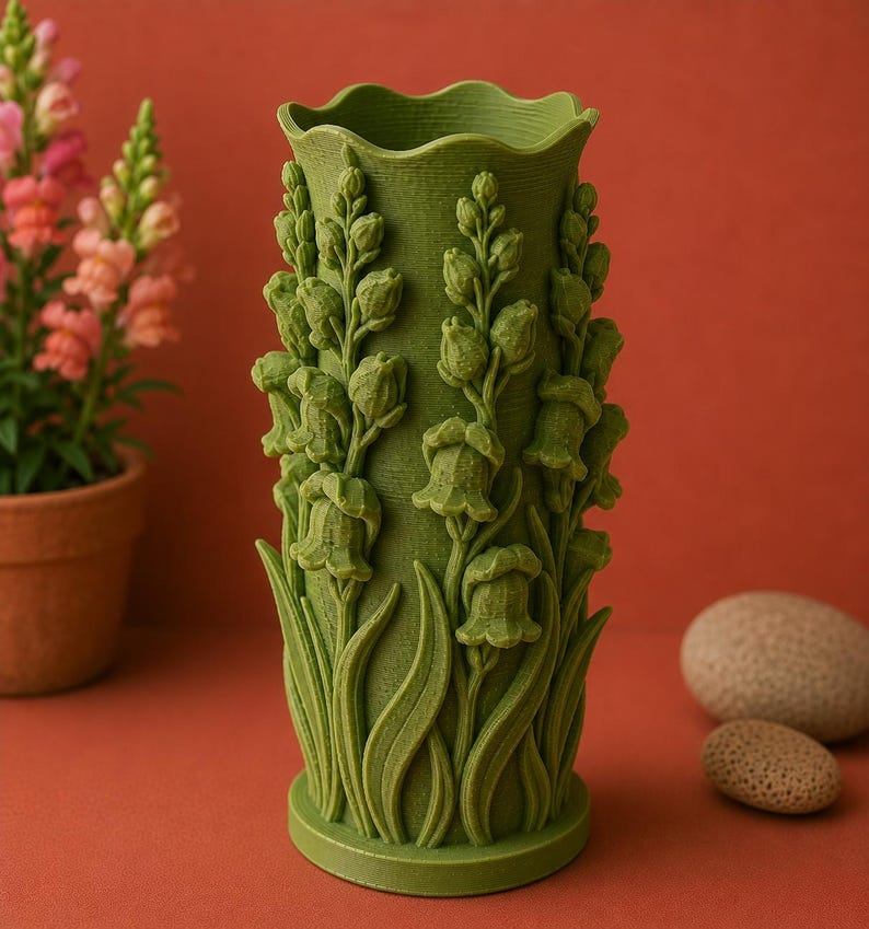 May include: A green vase with a floral design. The vase features detailed relief carvings of flowers and leaves. The vase has a wavy top edge and a cylindrical shape. The background is a solid reddish-orange color.