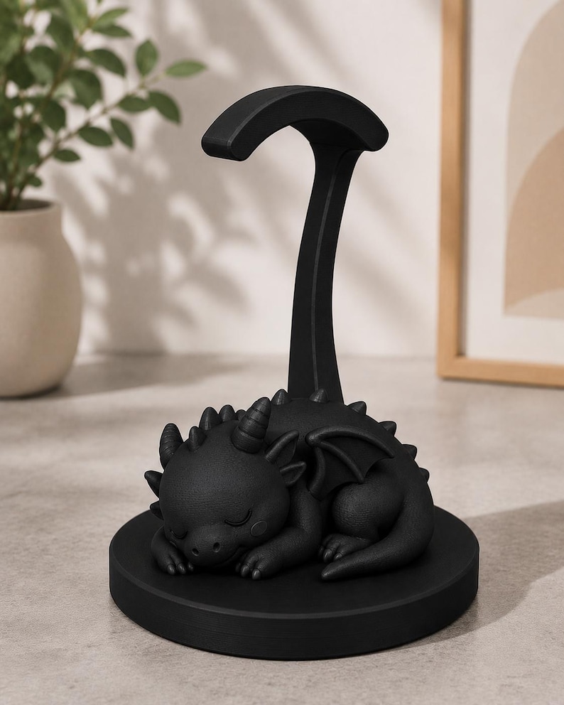 May include: A black dragon figurine resting on a round base, with a curved support extending upwards. The dragon has closed eyes, horns, and wings. The figurine is a decorative item.