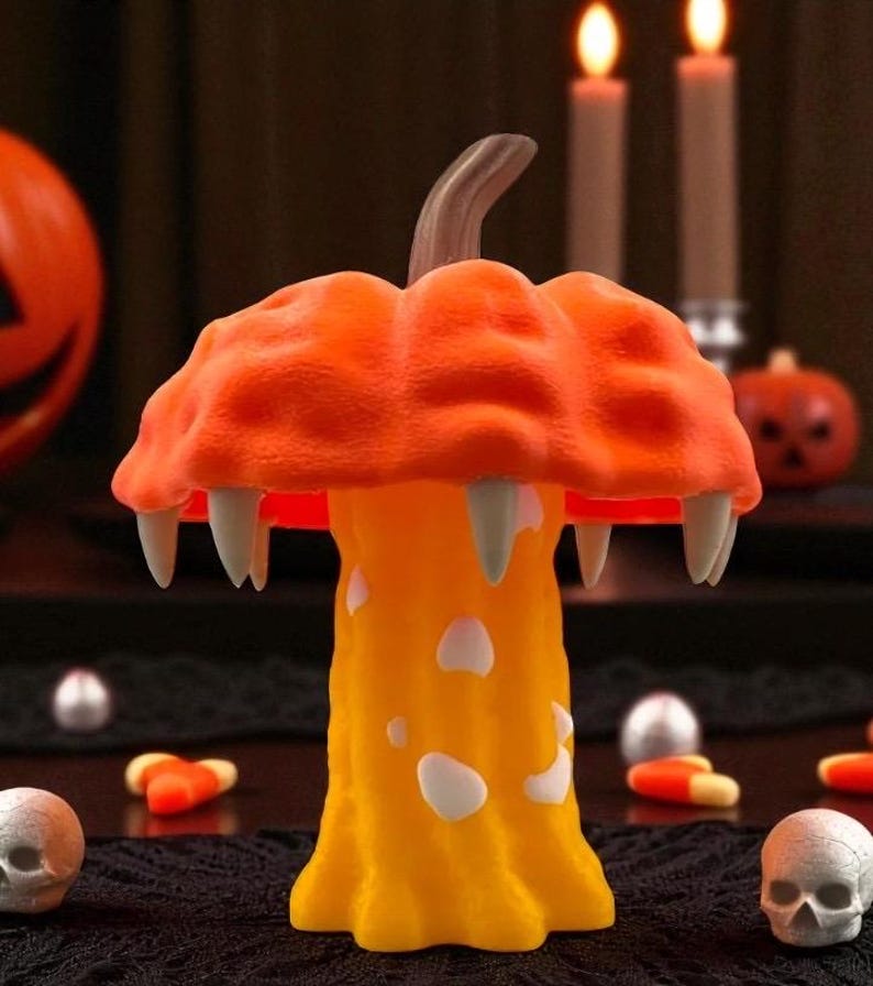 May include: A Halloween-themed decorative mushroom with an orange cap and yellow stem. The cap features fangs and the stem has white spots. The background includes candles, pumpkins, and skull decorations, creating a festive atmosphere.