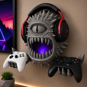 May include: A wall-mounted gray monster sculpture with a single eye and sharp teeth, featuring a glowing purple interior. The creature wears black and red over-ear headphones and has two clawed hands holding a white and a black game controller.