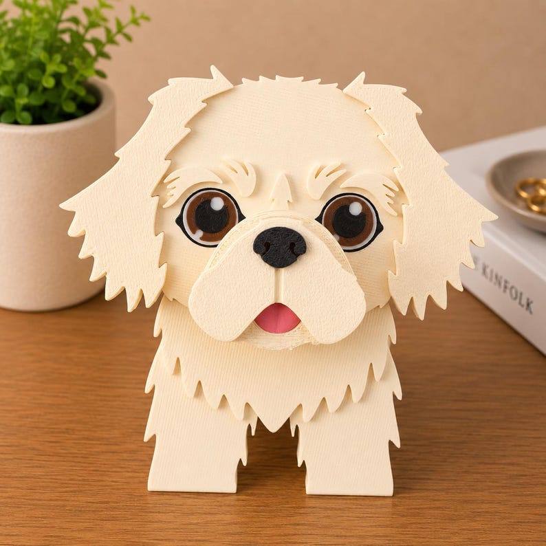 May include: A cream-colored, 3D papercraft dog figurine with large brown eyes, a black nose, and a pink tongue. The dog has detailed fur and is standing upright. The figurine is on a wooden surface.