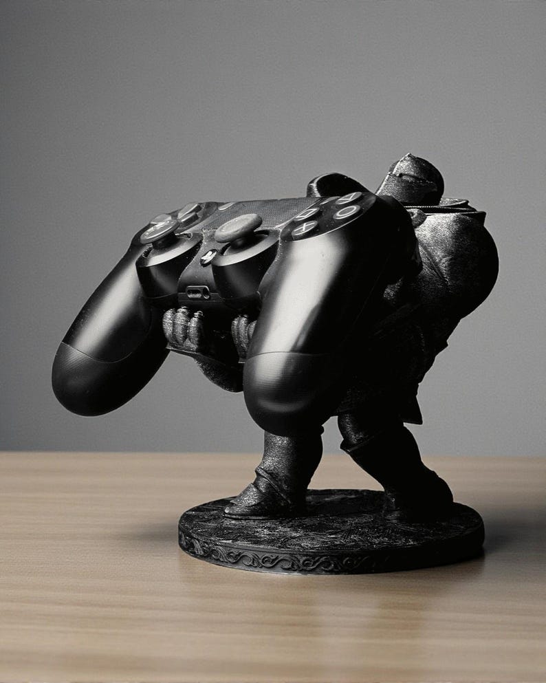 May include: A black sculpture of a knight holding a black video game controller. The knight is detailed with armor and stands on a decorative base. The controller features buttons and joysticks.