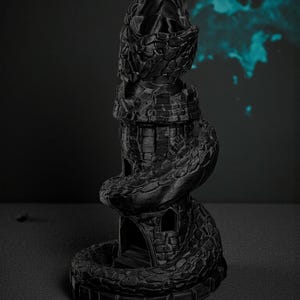 May include: A black, 3D-printed sculpture of a tower entwined by a snake. The tower has a castle-like design with windows and a textured surface. The snake wraps around the tower, adding a dynamic element to the piece. The sculpture is set against a dark background.