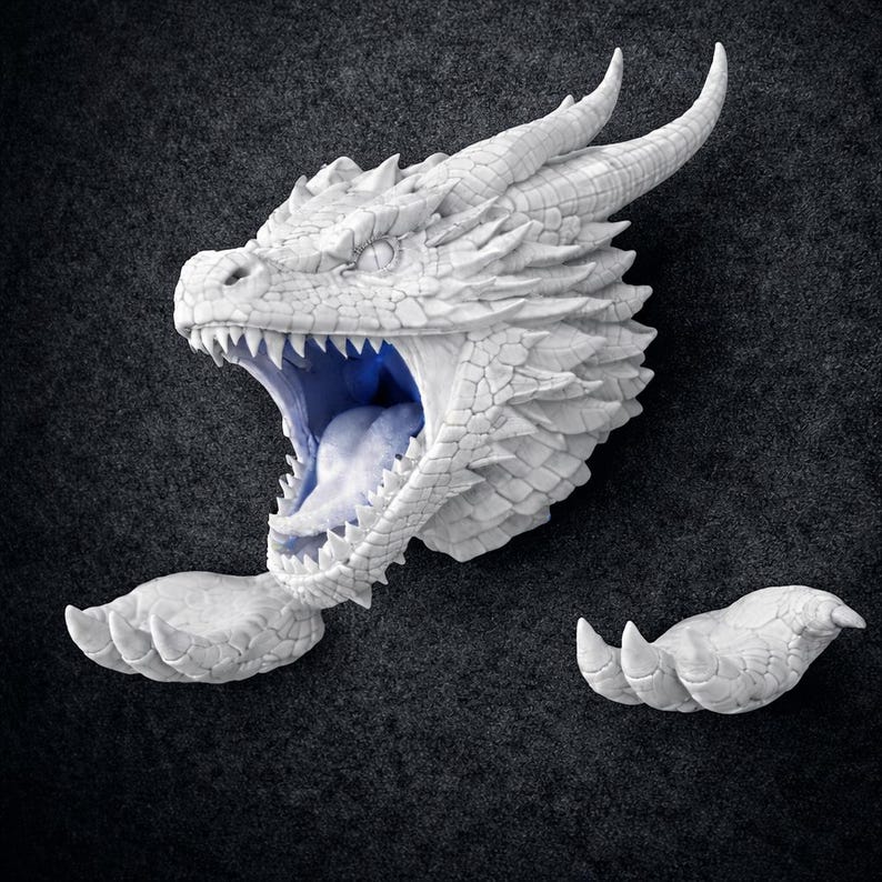 May include: A detailed, white dragon head sculpture with an open mouth revealing a blue interior. The sculpture includes horns, scales, and sharp teeth. Two detached dragon claws are also visible, all set against a dark gray background.