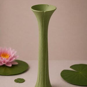 May include: A tall, green vase with a textured surface and a flared top. The vase is surrounded by green lily pads and a pink water lily. The vase is approximately 12 inches tall.