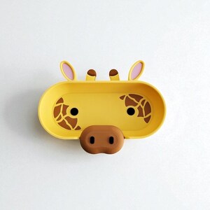 K&ouml;nnte beinhalten: Eine gelbe, ovale Seifenschale mit einem Giraffengesicht-Design. Die Schale hat braune Flecken, schwarze Augen und eine braune Nase. Die Ohren sind rosa. Die Schale ist auf einem wei&szlig;en Hintergrund montiert.