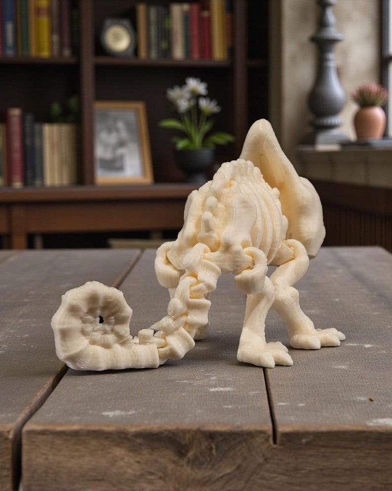 Op de afbeelding: Een cr&egrave;mekleurige, 3D-geprinte sculptuur van een fantastisch wezen met een schelpachtig lichaam, een gesegmenteerde staart en klauwpoten. De sculptuur wordt tentoongesteld op een houten oppervlak, waarbij het ingewikkelde ontwerp en de textuur worden getoond.