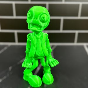 May include: A bright green 3D printed figurine of a skeleton wearing a suit and tie. The figurine has a comical expression and is posed with its arms outstretched.