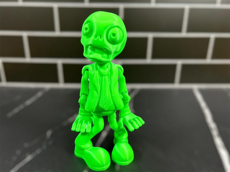 May include: A bright green 3D printed figurine of a skeleton wearing a suit and tie. The figurine has a comical expression and is posed with its arms outstretched.