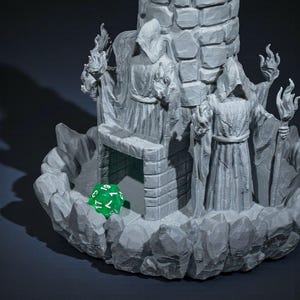 K&ouml;nnte beinhalten: Ein grauer, 3D-gedruckter Fantasy-W&uuml;rfelturm mit einem Steinturm, vermummten Figuren und einem gr&uuml;nen W&uuml;rfel. Der Turm hat ein detailliertes, strukturiertes Design mit Flammen und einem felsigen Sockel. Der W&uuml;rfel zeigt die Zahl 19.