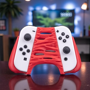 May include: A red and white video game controller accessory. The accessory has a textured red centre section with horizontal openings. The sides are white with black buttons and control sticks. The controller is designed to enhance the gaming experience.
