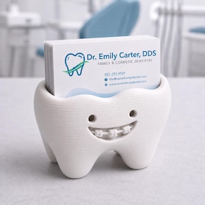 May include: A white, tooth-shaped business card holder with a smiling face and braces. The holder contains a stack of business cards for Dr. Emily Carter, DDS, Family & Cosmetic Dentistry. The background is a blurred dental office setting.