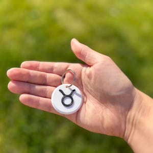 May include: White circular keyring with a black Taurus zodiac symbol.