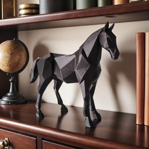 May include: A black geometric horse sculpture with a faceted design. The decorative horse statue is displayed on a dark wood surface, showcasing its modern aesthetic. The sculpture is a striking home decor accent.
