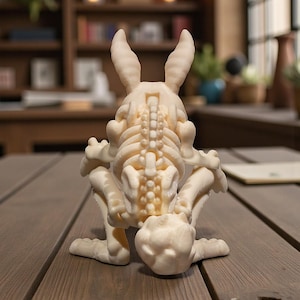 Puede incluir: Una escultura de esqueleto de conejo, impresa en 3D, de color crema. La escultura est&aacute; en posici&oacute;n agachada, con las orejas erguidas. Los detalles de la caja tor&aacute;cica, la columna vertebral y las extremidades son visibles. Sobre una superficie de madera.