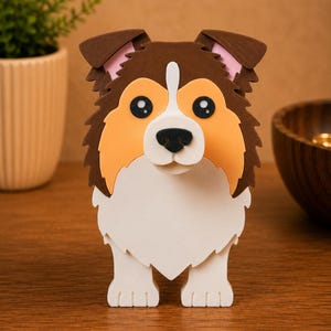 May include: A layered, three-dimensional dog figurine with a brown, tan, and white color scheme. The dog has large, black eyes, a white muzzle, and a fluffy, textured appearance. The figurine is standing upright.