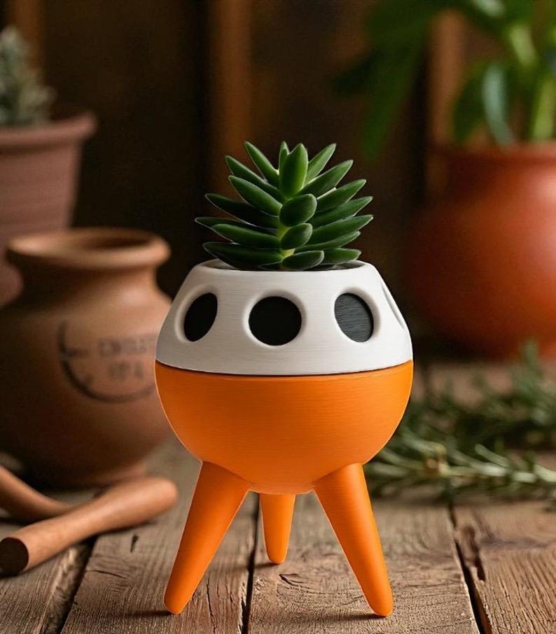May include: A unique, orange and white rocket-shaped planter with three legs, holding a green succulent plant. The planter has three black circular openings on the white upper section. The planter sits on a wooden surface.