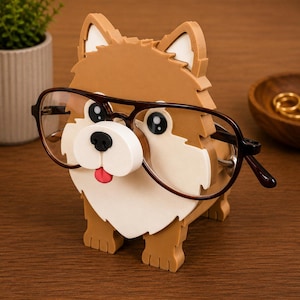 May include: A brown and white dog-shaped eyeglasses holder with a black nose, black eyes, and a red tongue. The holder is wearing a pair of brown-rimmed glasses. The holder is made of wood and is sitting on a wooden surface.