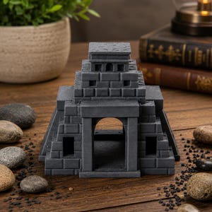 Puede incluir: R&eacute;plica gris en miniatura de un templo con dise&ntilde;o escalonado. El modelo presenta una entrada arqueada, ventanas rectangulares y un techo plano. La estructura est&aacute; hecha de un material similar a la piedra y se asienta sobre una superficie de madera.