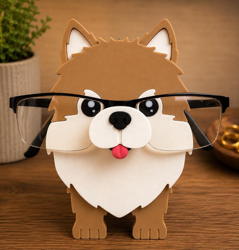 May include: A brown, white, and black dog-shaped eyeglasses holder with a pink tongue sticking out. The holder has black-framed glasses resting on it. The holder is made of a sturdy material and is designed to hold eyeglasses.