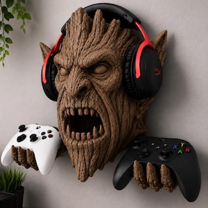 May include: A wall-mounted brown tree-like creature sculpture with a textured bark surface, pointed ears, and an open mouth. The sculpture features two hands extending outward to hold a white game controller and a black game controller.