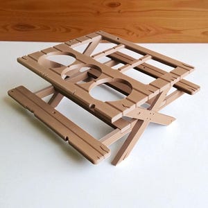 Puede incluir: Una mesa de picnic de madera marr&oacute;n con un dise&ntilde;o &uacute;nico. La mesa tiene una parte superior rectangular con cuatro recortes circulares y una base plegable. La mesa est&aacute; hecha de madera y tiene un aspecto r&uacute;stico. La mesa est&aacute; dise&ntilde;ada para sostener bebidas.