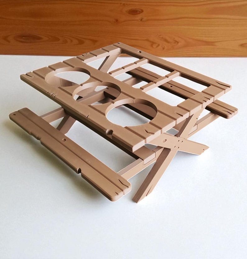 Puede incluir: Una mesa de picnic de madera marr&oacute;n con un dise&ntilde;o &uacute;nico. La mesa tiene una parte superior rectangular con cuatro recortes circulares y una base plegable. La mesa est&aacute; hecha de madera y tiene un aspecto r&uacute;stico. La mesa est&aacute; dise&ntilde;ada para sostener bebidas.