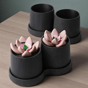 May include: Four dark gray ceramic planters with a ribbed texture. Two planters contain artificial succulents with pink petals and green centers. The planters sit on matching saucers, and are arranged on a wooden surface.