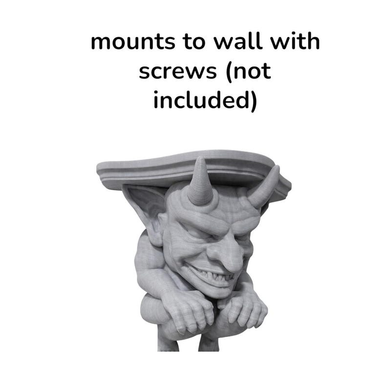 K&ouml;nnte beinhalten: Graue Gargoyle-Regalhalterung mit teuflischem Design. Die Halterung hat H&ouml;rner und ein grimmiges Gesicht und ist f&uuml;r die Wandmontage mit Schrauben vorgesehen. Der Text "mounts to wall with screws (not included)" befindet sich &uuml;ber dem Gargoyle.
